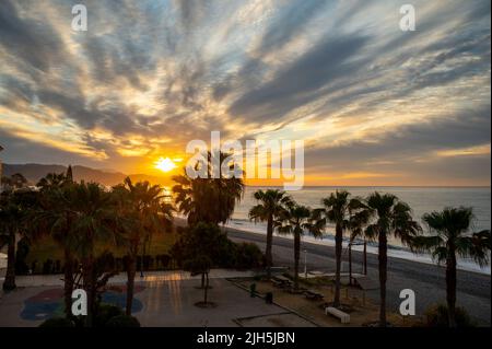 Sonnenaufgang über Meerwasser und Palmen in Torrox Costa, Costa del Sol, kleiner touristischer Ort zwischen Malaga und Nerja, Andalusien, Spanien Stockfoto