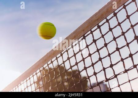 Tennisball fliegt dicht über das Netz, gefährlicher Treffer, Ball ist in Bewegung, der Himmel ist auf dem Hintergrund, Blick von unten. Stockfoto