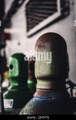 Druckgasflaschen, die vertikal durch eine Metallkette und eine Metallkappe gesichert gelagert werden. Stockfoto