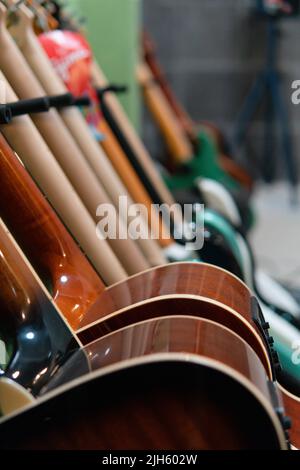 Akustische und elektrische Gitarren auf einem Regal angeordnet. Gitarrendisplay. Gitarren in verschiedenen Farben in einem Music Store arrangiert. Musikstudio mit verschiedenen Gitarren. Teile des Körpers der Gitarren. Stockfoto