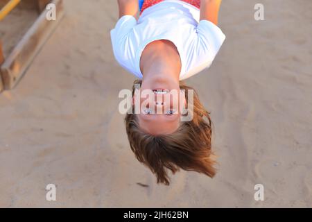 Das Mädchen reitet auf einer Schaukel auf dem Spielplatz. Karussells für Kinder im Freien Stockfoto