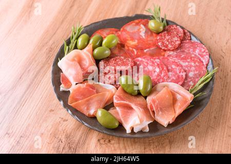 Wurstplatte mit Fleischvorspeise, verschiedene Würste - Salami, bresaola, Proscuitto serviert mit Oliven und Kräutern. Schwarze Platte mit traditionellem I Stockfoto