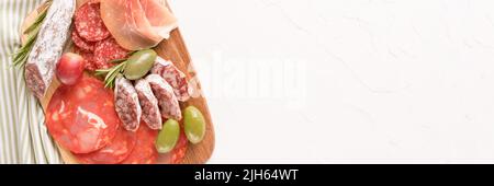 Banner mit Wurstplatte mit verschiedenen Wurstsorten - Salami, Bresaola, Proscuitto serviert mit Oliven und Crackern. Hintergrund des Bannermenüs Stockfoto