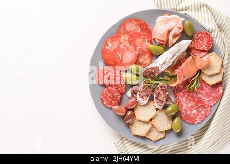 Wurstplatte mit Wurstsorten - Salami, Bresaola, Proscuitto, serviert mit Oliven und Crackern auf weißem Tisch. Menühintergrund mit Kopie Stockfoto