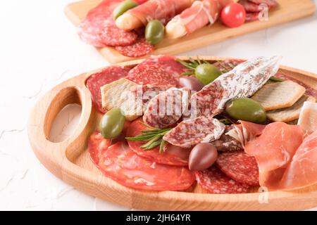 Charcuterie-Tafel mit Würstensorten - Salami, Bresaola, Proscuitto, serviert mit Oliven und Crackern auf weißem Tisch. Menühintergrund mit Kopie Stockfoto