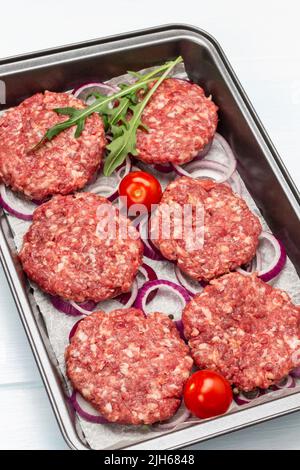 Rohe Rindfleisch-Burger mit gehackten Zwiebeln und Tomaten auf dem Backblech. Draufsicht. Weißer Hintergrund Stockfoto