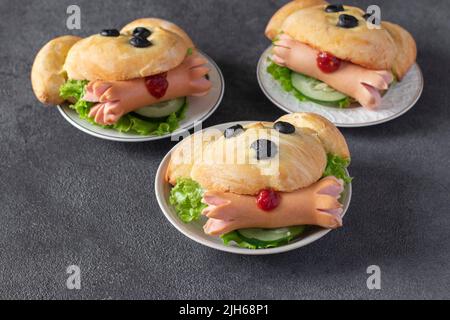 Fun Food für Kinder - drei Sandwiches in Form eines Hundes mit Würstchen und Gurken auf dunkelgrauem Hintergrund Stockfoto