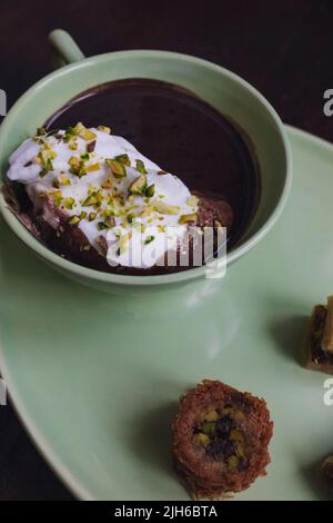 Heiße Schokolade in passendem grünen Becher und Teller mit verschiedenen Baklava-Desserts trinken Stockfoto