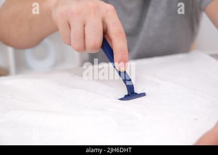 Ein Mann entfernt Stofftabletten mit einer Einweg-Rasiermaschine. Ein Rasiermesser zum Entfernen von Pellets. Stockfoto