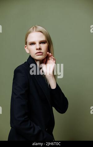 Cooles Banner für Marken. Ein attraktives, cooles Profi-Model posiert in einer Halbdrehung und blickt auf einem grünen olivgrünen Hintergrund im Studio auf die Kamera Stockfoto