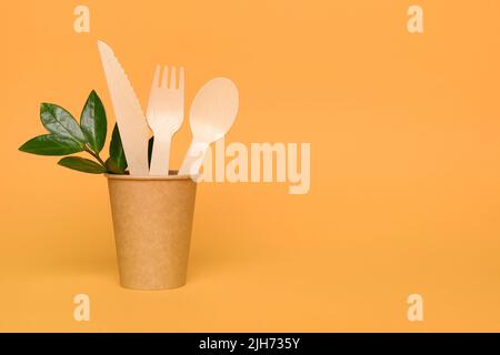 Natürliches Bambus-Holzbesteck in Papiertasse - biologisch abbaubares und kompostierbares Besteck- und Geschirrkonzept. Bambus Besteck vor orangefarbenem Hintergrund Stockfoto