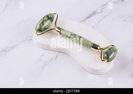 Jade Face Roller gua Sha für Gesichtsmassage über weißem Marmortisch. Gesichtsmassage-Werkzeug für die Lifting-Therapie aus Natursteinen. Hautpflegewerkzeuge Stockfoto