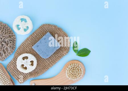 Natürliches Badezubehör für Körperpflege und Schrubben auf blauem Hintergrund - Holzbürste, Körperpeeling, Loofah-Schwamm, natürliches Hanf-Badetuch und Bad Stockfoto