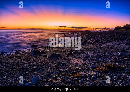 Spektakulärer, farbenfroher Sonnenaufgang über dem pazifischen Ozeanhorizont am Kieselstrand in Forster, der Stadt Australiens. Stockfoto