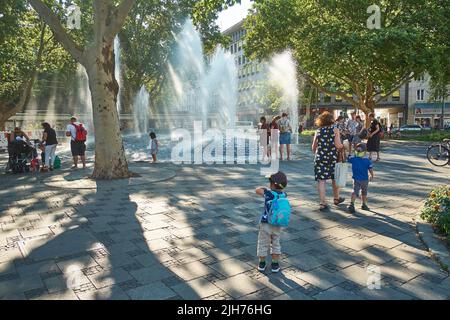 Familien genießen einen frischen Springbrunnen im außergewöhnlich warmen Sommer von München. Der Klimawandel hat München heißere Sommer gebracht. Stockfoto