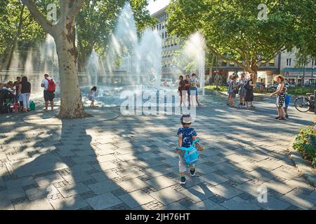 Familien genießen einen frischen Springbrunnen im außergewöhnlich warmen Sommer von München. Der Klimawandel hat München heißere Sommer gebracht. Stockfoto