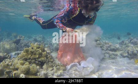 Frau in Tauchausrüstung schwimmt und sammelt Plastikmüll unter Wasser auf dem Boden des Korallenriffs. Schnorchler reinigt Ozean von Plastikverschmutzung. P Stockfoto