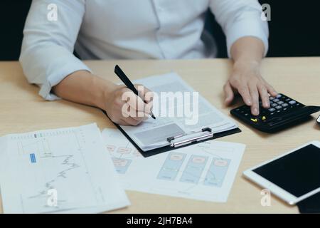 Nahaufnahme. Die Hände eines jungen Mannes ein Buchhalter in einem weißen Hemd, der an einem Schreibtisch mit Dokumenten, einem Taschenrechner, arbeitet, schreibt. Sitzen in einem modernen Büro Stockfoto