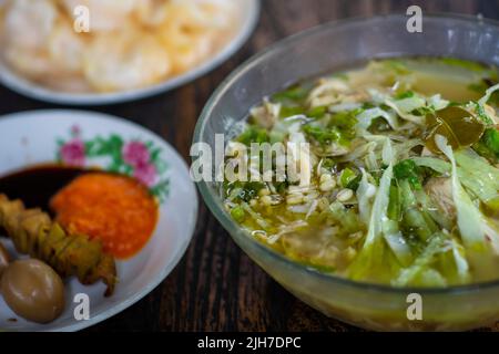 Soto Kudus ist eine indonesische Delikatesse, Hühnersuppe mit unscharfem Hintergrund indonesischer Cracker (Krupuk) Stockfoto