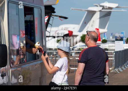 RAF Fairford, Gloucestershire, Großbritannien. 16. Juli 2022. Eine der größten Airshows der Welt ist nach einer 3-jährigen Pause zurückgekehrt, da die covid Pandemie internationale Luftstreitkräfte, Display-Teams und riesige Menschenmengen in die Cotswolds brachte. Ein Mädchen kauft ein Eis von einem Händler, wobei Flugzeuge ausgestellt sind Stockfoto