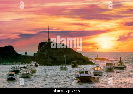 Nach einem sehr heißen Julitag an der Küste Cornichs wird der Himmel in Rosa- und Orangetönen, während sich die Menschen versammeln, um den Sonnenuntergang durch den Dunst am zu beobachten Stockfoto