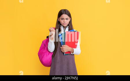 Wütendes Kind mit Schulrucksack und Arbeitsbuch auf gelbem Hintergrund Stockfoto