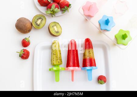 Weißer quadratischer Teller mit buntem hausgemachtem Kiwi- und Erdbeereis auf einem weißen Tisch Stockfoto