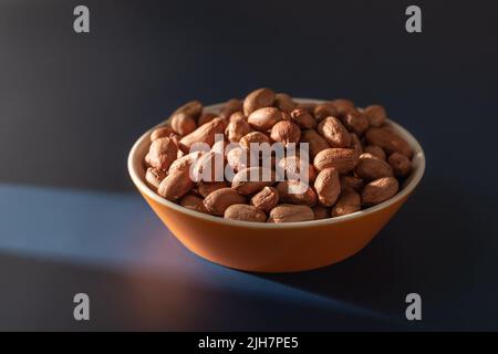 Getrocknete Bio-Erdnuss in einer Glasschale vor dunkelblauem Hintergrund. Getrocknete Affenmutter für einen verzehrfertigen vegetarischen Snack. Rohe geschälte Erdnuss. Stockfoto