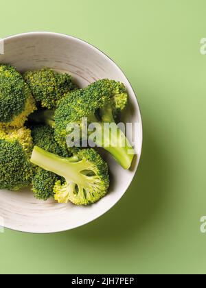 Roher Brokkoli blühte ganz und halbierte sich in einer Schüssel vor pastellgrünem Hintergrund. Kalorienarme antioxidative Detox-Diät und vegetarische Vitaminnahrung. Stockfoto