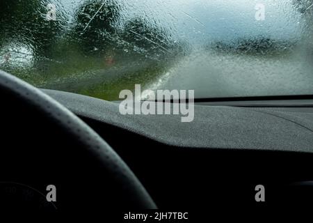 Fahren des Autos auf der Autobahn bei starkem Regen. Blick von der Frontscheibe auf die Straße. Windschutzscheibe voller verschwommener Regentropfen. Stockfoto