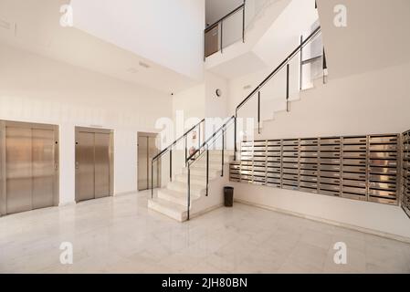 Lobby eines Gebäudes mit Atrium, Treppen mit Metall- und Glasgeländern, Briefkästen aus Edelstahl und einer Batterie mit drei Aufzügen Stockfoto