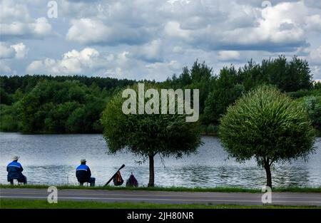 Zwei Männer in blauen Jacken fischen zusammen mit einer Angelrute am Ufer eines Sees. Stockfoto