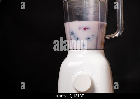 Milchshake in einer Schüssel mit einem Mixer aus Milch, Erdbeeren und Brombeeren auf schwarzem Hintergrund, ein Ort für Text Stockfoto