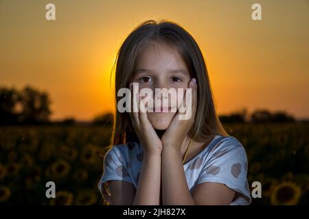 Ein kleines Mädchen hält ihren Kopf in den Händen vor dem Hintergrund des Sonnenuntergangs Stockfoto