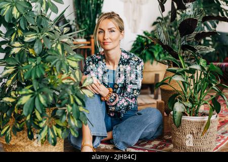 Porträt einer jungen Frau, die auf dem Boden sitzt und von Topfpflanzen umgeben ist. Stockfoto