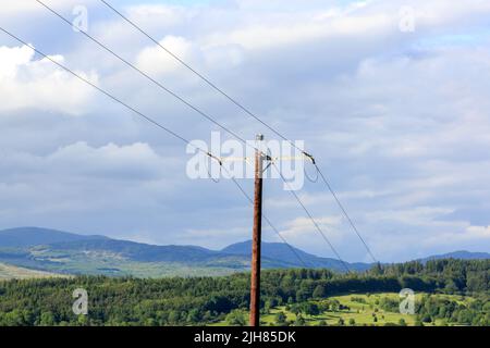 Stromkabel, die auf einer Holzpoll mit der schottischen Landschaft im Hintergrund befestigt sind Stockfoto