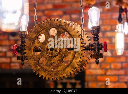 Steampunk Design-Element im architektonischen Stil des Innenraums. Lampen, die auf Zahnrädern mit Eisenzahnrädern befestigt sind, beleuchteten Geräte, die in Innenräumen hängen Stockfoto