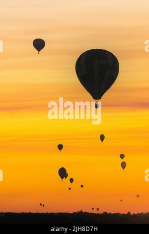 Heißluftballons werden bei Sonnenuntergang in einem zusammengesetzten Bild gegen den Himmel geschildet. Stockfoto