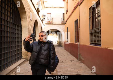 Eine junge attraktive lateinische nicht-binäre Person, die Make-up und warme Kleidung trägt und Selfie mit einem Telefon macht Stockfoto