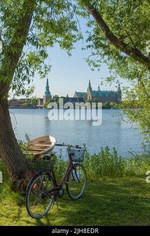 Eine vertikale Aufnahme eines Fahrrads am Ufer eines Sees mit Schloss Frederiksborg im Hintergrund Stockfoto