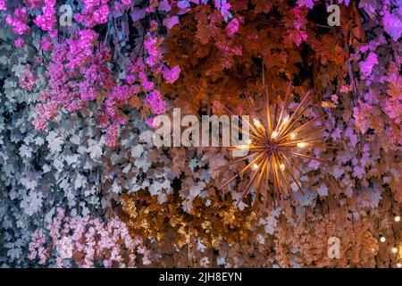 Ein malerischer Blick auf einen glänzenden Kronleuchter, der an einer Decke hängt und von Blumenschmuck umgeben ist Stockfoto