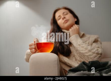 Frau sitzt zu Hause auf dem Sofa ungesund mit einer Tasse heißen Tee. Stockfoto