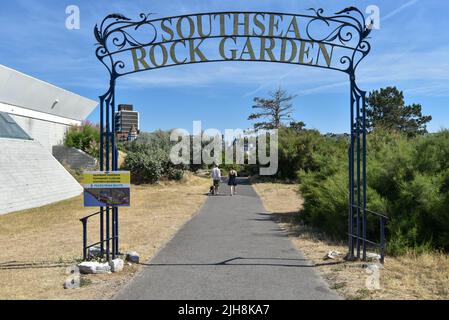 Ein paar Leute laufen mit ihrem Hund durch den Eingang zu den Southsea Rock Gardens in Portsmouth, England. Stockfoto