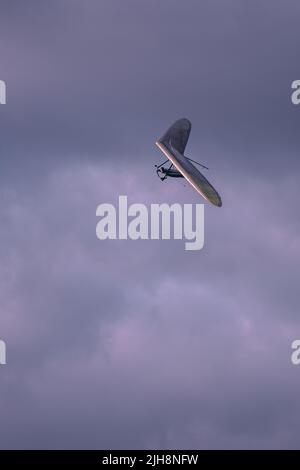 Eine vertikale Aufnahme eines Hängegleiters, der in den trüben grauen Himmel fliegt Stockfoto