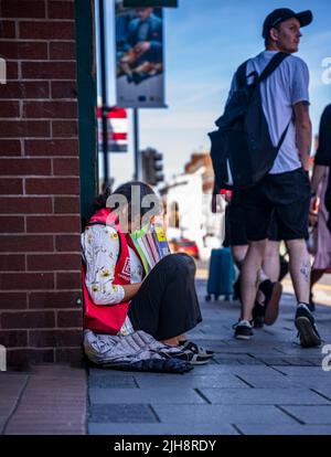 Grantham, Lincolnshire, Großbritannien – Eine junge asiatische Frau saß auf dem Straßenweg und verkaufte Kopien von The Big Issue, während die Leute an ihr vorbeigingen und sie ignorierten Stockfoto