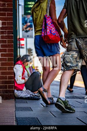 Grantham, Lincolnshire, Großbritannien – Eine junge asiatische Frau saß auf dem Straßenweg und verkaufte Kopien von The Big Issue, während die Leute an ihr vorbeigingen und sie ignorierten Stockfoto