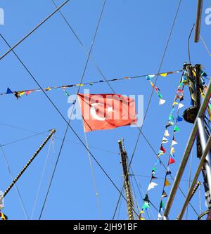 Eine türkische Flagge auf einem Schiff unter den Segelmasten, blauer Himmel im Hintergrund. Türkei Flagge winkt im Wind auf einem Meeresgrund. Türkische Flagge an Bord des Schiffes. Stockfoto