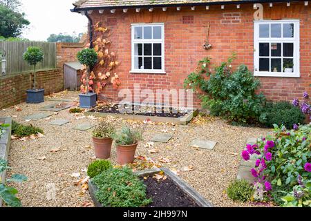 Herbstgarten in England, Großbritannien. Harte Landschaftsgestaltung mit Kies, York Steinplatten und Eichenholzbetten mit erhöhten Betten Stockfoto