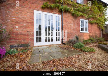Fenstertüren aus Holz und eine Terrasse aus York-Stein in einem britischen Landschaftsgarten mit Herbstblättern Stockfoto