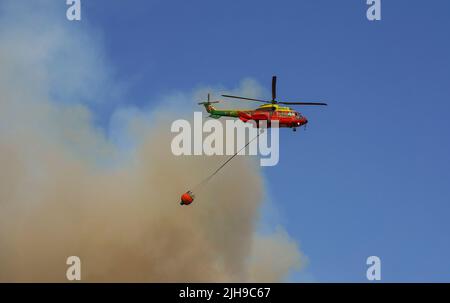 Mittelgroßer Hubschrauber von INFOCA, der einen Wassereimer trägt, um auf ein Waldfeuer zu fallen, Mijas, Spanien. Stockfoto